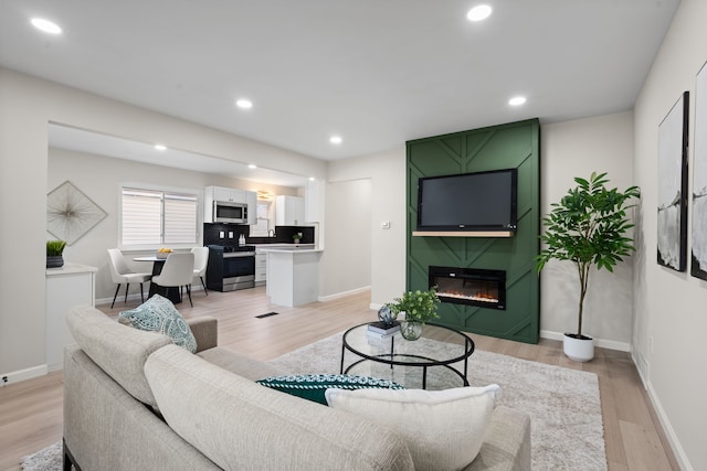 living room featuring light wood-type flooring, baseboards, a large fireplace, and recessed lighting
