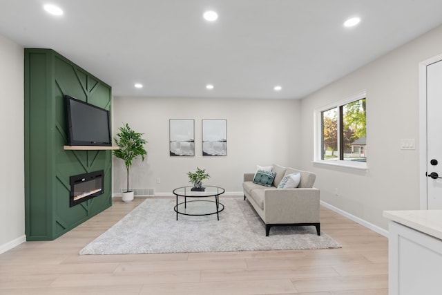 living room featuring light wood-type flooring, baseboards, a fireplace, and recessed lighting