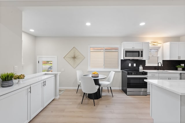 kitchen with appliances with stainless steel finishes, a sink, light wood-style floors, white cabinetry, and tasteful backsplash