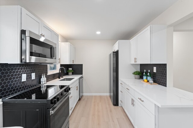 kitchen with appliances with stainless steel finishes, a sink, light wood finished floors, recessed lighting, and backsplash