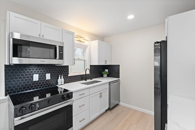 kitchen with appliances with stainless steel finishes, a sink, decorative backsplash, light wood-style floors, and white cabinetry