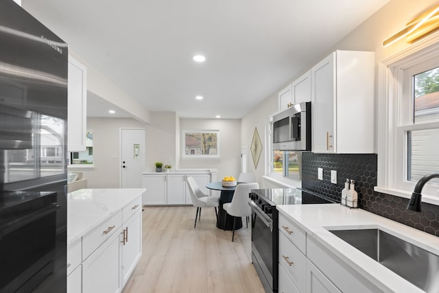 kitchen with electric range oven, stainless steel microwave, a sink, tasteful backsplash, and light wood-style flooring