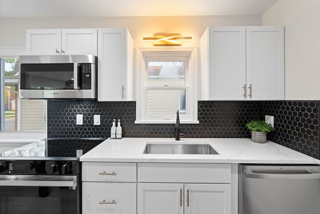 kitchen with stainless steel appliances, a sink, backsplash, and white cabinets