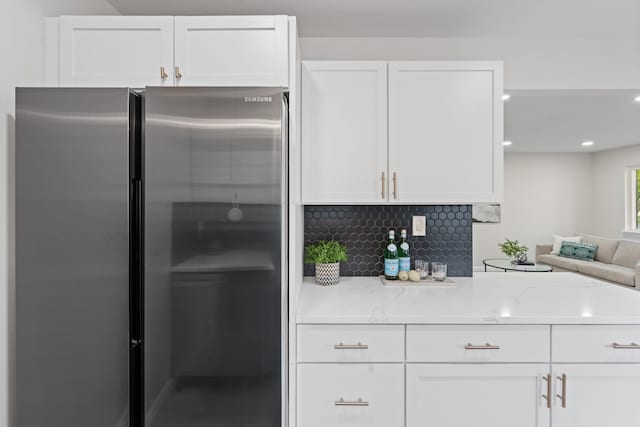 kitchen with freestanding refrigerator, white cabinetry, decorative backsplash, light stone counters, and open floor plan