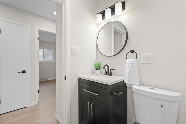 bathroom featuring vanity, baseboards, wood finished floors, and toilet