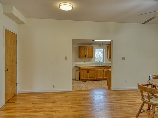 kitchen featuring brown cabinets, light countertops, baseboards, a sink, and light wood-style floors