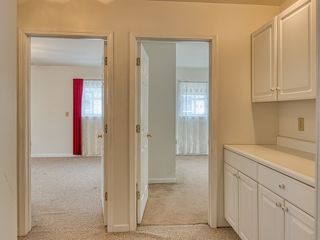 hallway with baseboards and light carpet