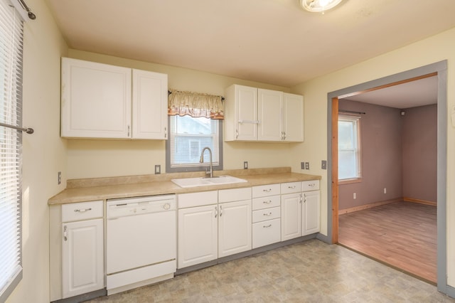kitchen with white dishwasher, a sink, white cabinets, and light countertops