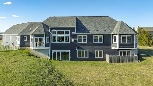 back of property with fence, a shingled roof, and a yard