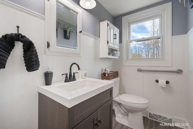 half bathroom featuring vanity, toilet, wood finished floors, and visible vents