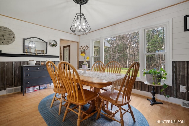 dining space with wood walls, light wood-style flooring, and visible vents