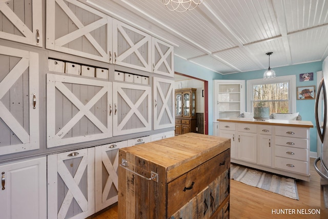 kitchen featuring a center island, hanging light fixtures, light wood finished floors, wood counters, and white cabinetry