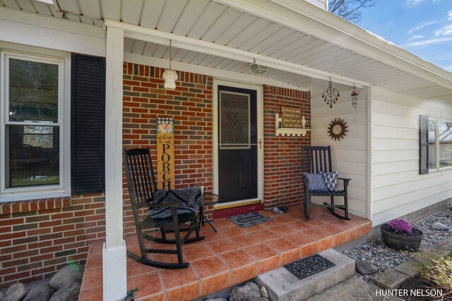 view of exterior entry featuring covered porch and brick siding