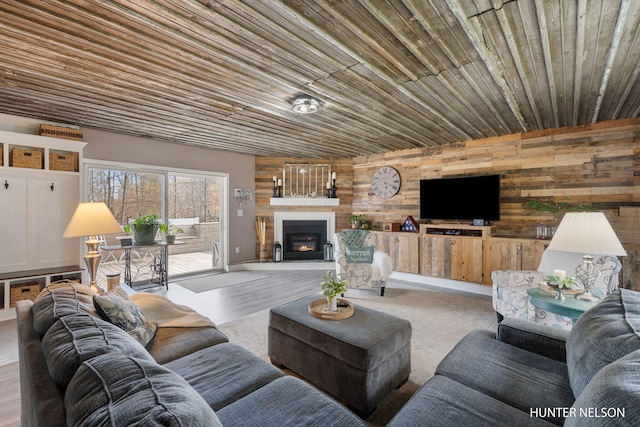 living room featuring wooden walls, wood ceiling, a warm lit fireplace, and wood finished floors