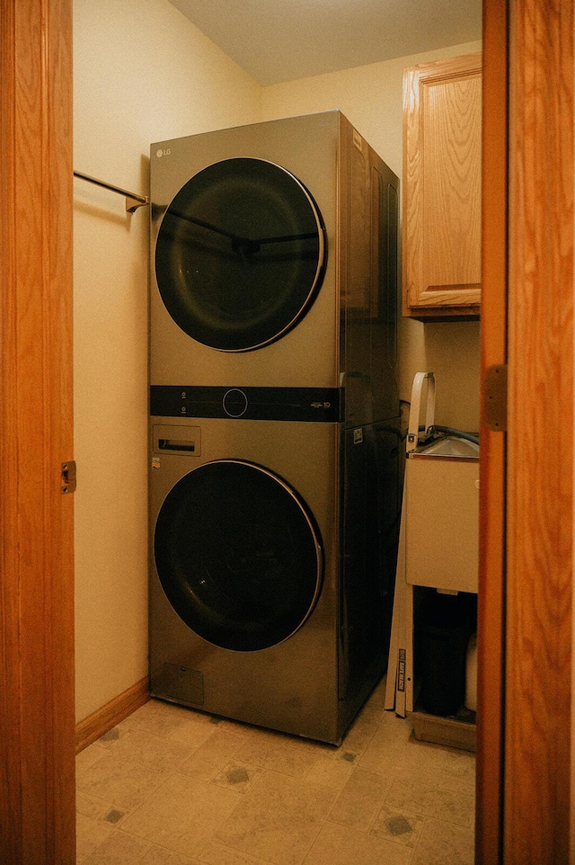 clothes washing area featuring a sink, stacked washer and dryer, and cabinet space