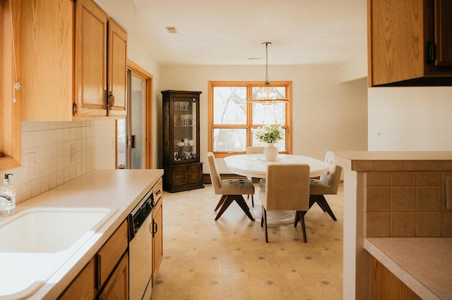 kitchen with tasteful backsplash, dishwasher, a sink, light countertops, and light floors
