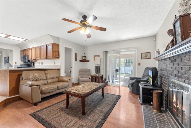 living room with light wood-style floors, ceiling fan, a brick fireplace, and a textured ceiling