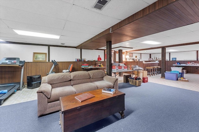 carpeted living room with a wainscoted wall, visible vents, wood walls, and a paneled ceiling