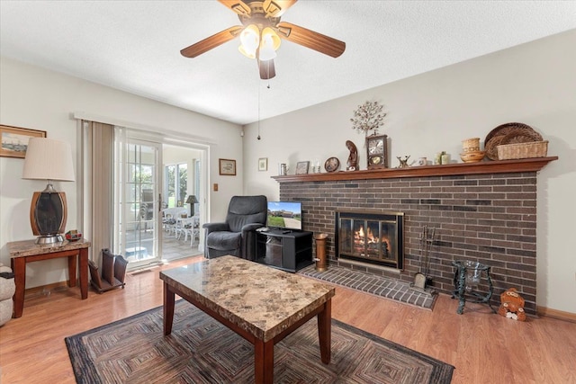 living area featuring light wood-style floors, ceiling fan, and a brick fireplace