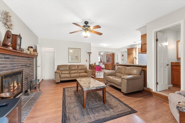 living area featuring light wood-type flooring, ceiling fan, and a fireplace