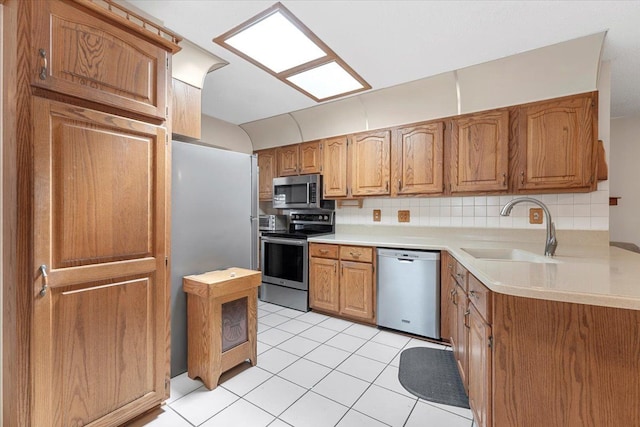 kitchen with light countertops, brown cabinets, a sink, light tile patterned floors, and stainless steel appliances