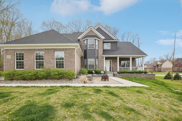 view of front facade with roof with shingles, an outdoor fire pit, brick siding, a front yard, and a patio area