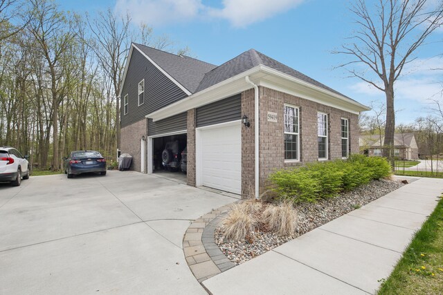 view of side of home with roof with shingles, an attached garage, concrete driveway, and brick siding