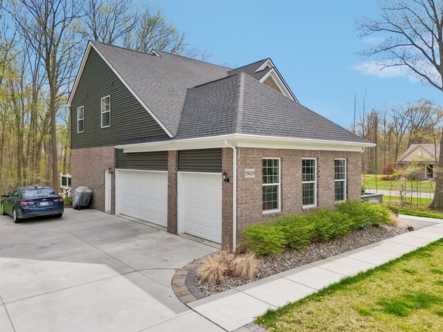 view of property exterior with roof with shingles, an attached garage, driveway, and brick siding