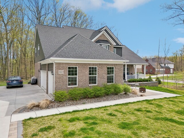 view of front facade featuring covered porch, driveway, a front lawn, and brick siding