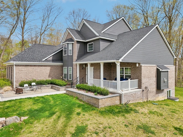 traditional-style house with brick siding, a front lawn, an outdoor fire pit, and roof with shingles