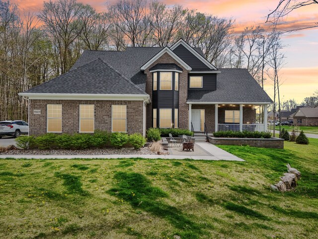 view of front facade with a lawn, brick siding, a fire pit, and roof with shingles