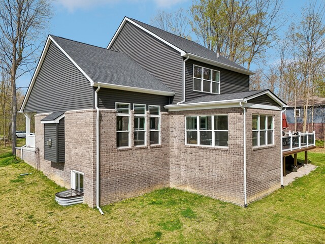 view of side of property with a lawn, brick siding, a wooden deck, and a shingled roof