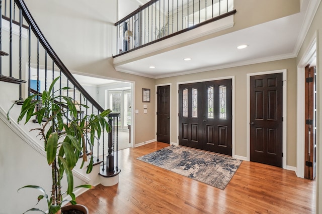 foyer entrance featuring crown molding, a towering ceiling, wood finished floors, and stairway
