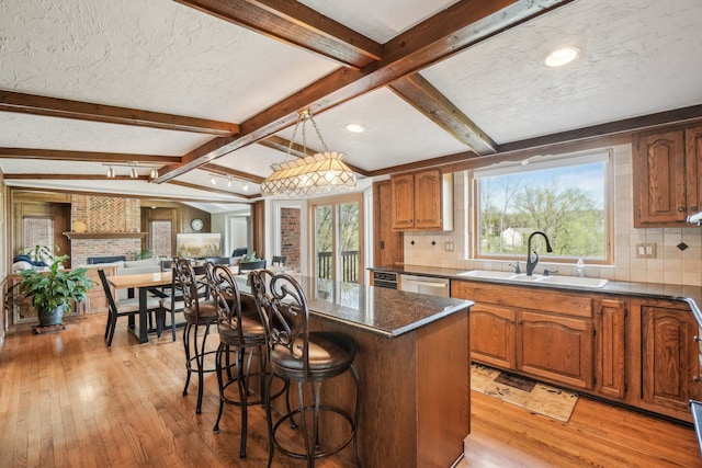 kitchen featuring a breakfast bar, a sink, light wood finished floors, backsplash, and beamed ceiling