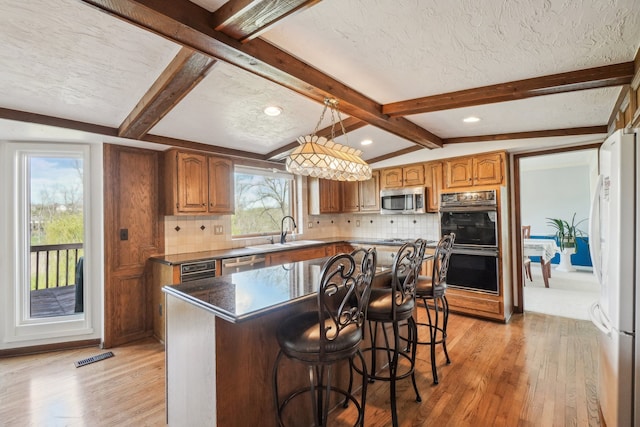kitchen with brown cabinetry, a sink, light wood-style flooring, appliances with stainless steel finishes, and backsplash
