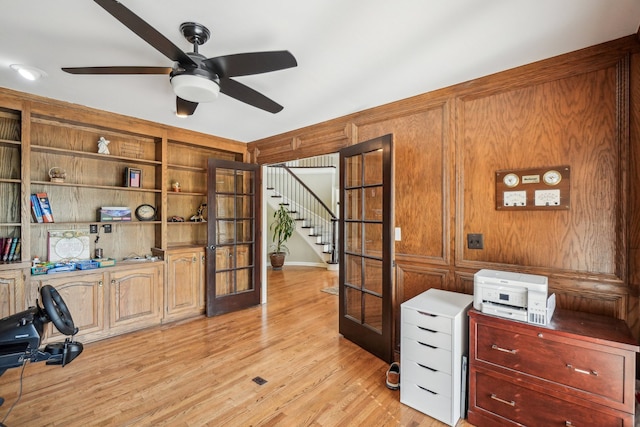 home office with french doors, light wood-style floors, a ceiling fan, and wooden walls