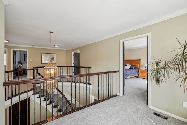 hallway featuring visible vents, ornamental molding, baseboards, carpet flooring, and an upstairs landing