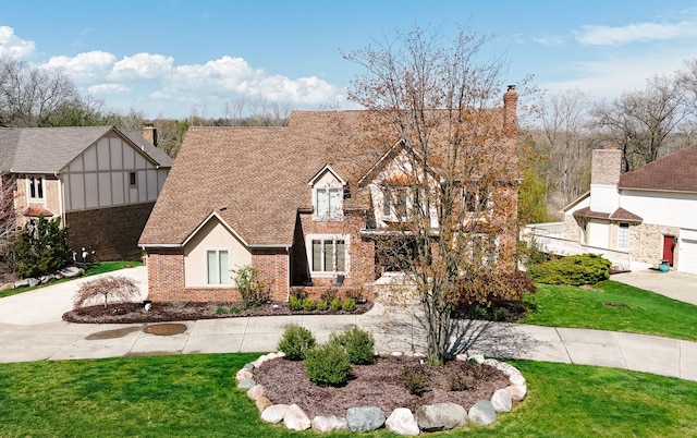 tudor home with brick siding, a front lawn, and roof with shingles