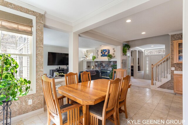 dining room featuring crown molding, marble finish floor, a glass covered fireplace, baseboards, and arched walkways