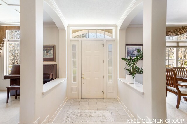 foyer entrance with crown molding, arched walkways, and a healthy amount of sunlight