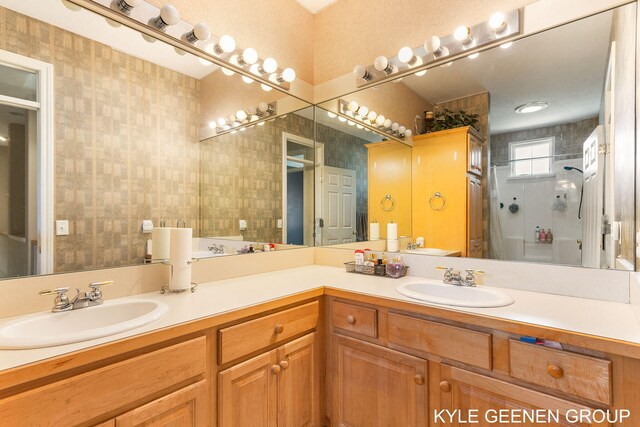 full bath featuring a sink, a shower, wallpapered walls, and double vanity