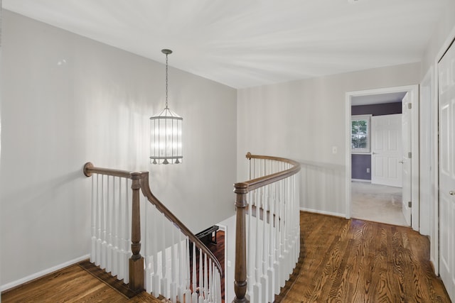 corridor with a notable chandelier, an upstairs landing, and wood finished floors