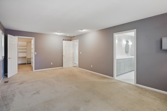 unfurnished bedroom with baseboards, a spacious closet, and light carpet