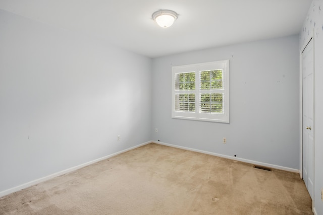 empty room with baseboards, visible vents, and light carpet