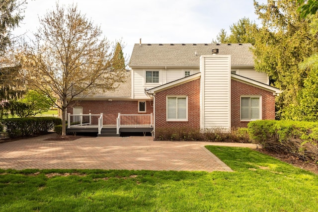 rear view of property with a chimney, a lawn, a wooden deck, brick siding, and a patio