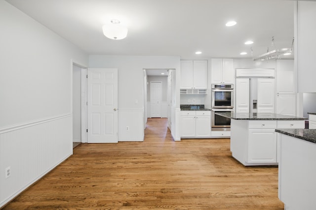 kitchen featuring wainscoting, double oven, light wood-style floors, a center island, and white cabinetry
