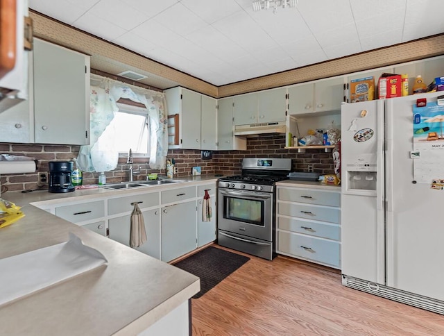 kitchen featuring light wood-style floors, stainless steel gas range oven, under cabinet range hood, a sink, and white fridge with ice dispenser