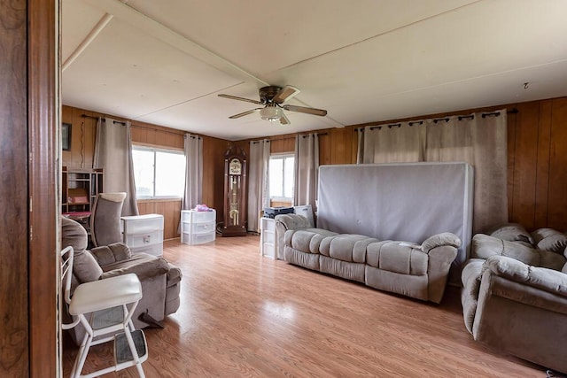 living area with a ceiling fan, wood walls, and light wood-style floors