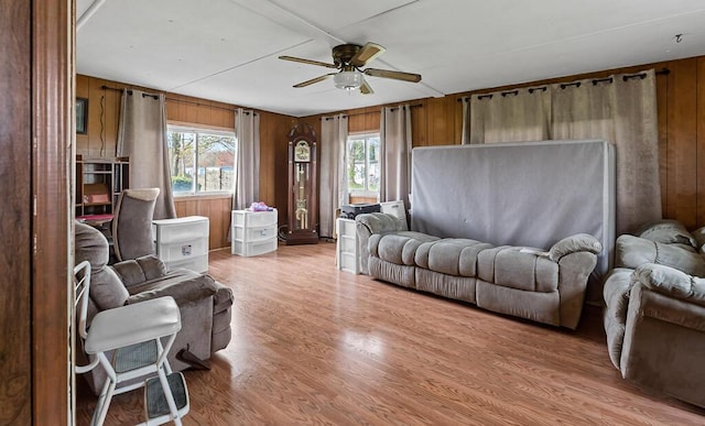 living area with light wood-type flooring, a ceiling fan, wooden walls, and a wealth of natural light