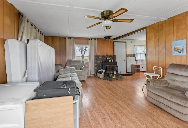 living room featuring light wood-style floors, ceiling fan, a wood stove, and wood walls